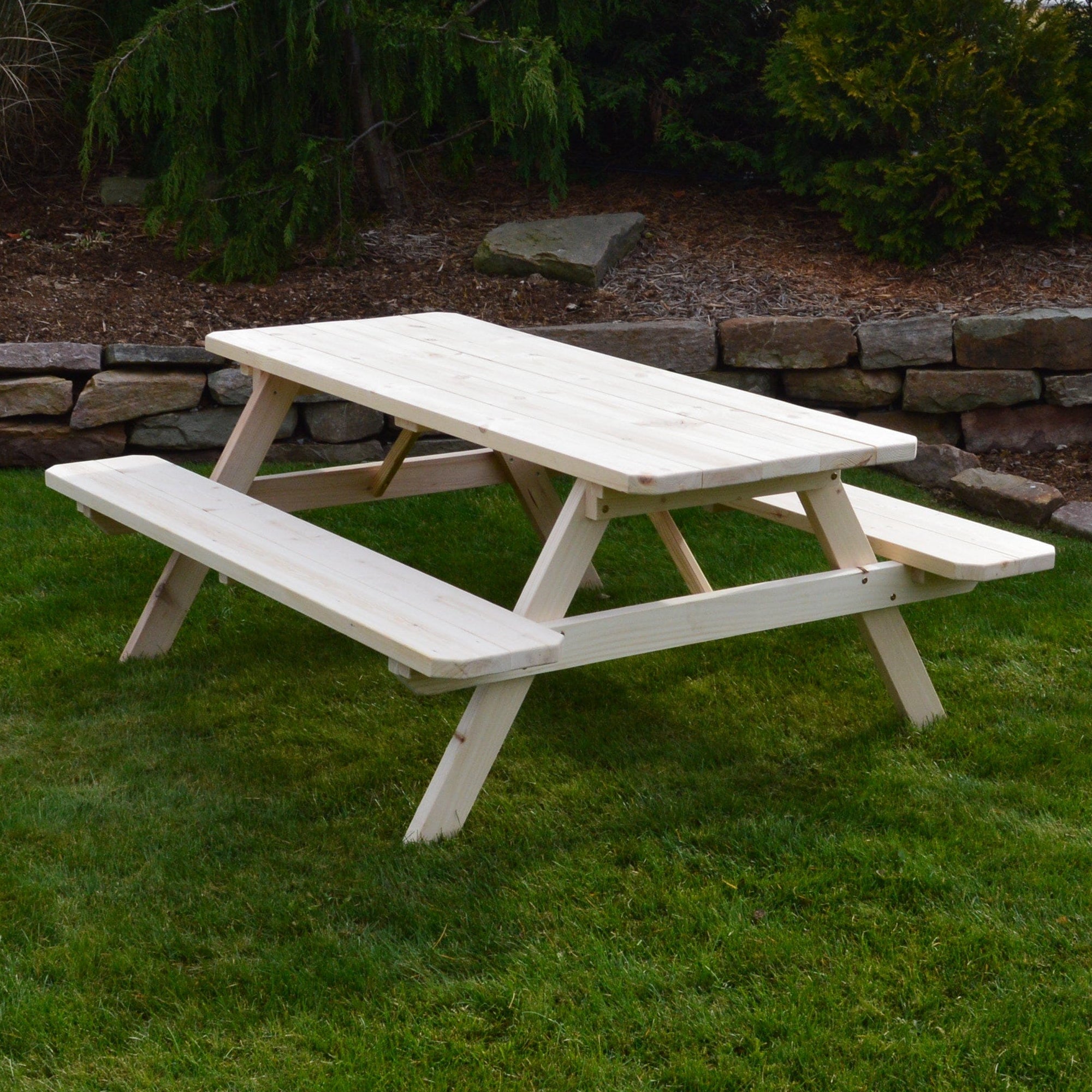 Wooden picnic table on a grassy area with trees and rocks in the background